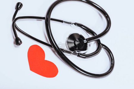 Téléchargez les photos : Un stéthoscope noir est isolé sur un fond blanc avec un cœur rouge comme symbole de cardiologie. Photo conceptuelle de la santé cardiaque. - en image libre de droit