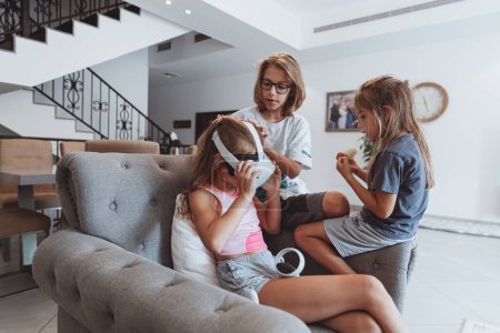 Téléchargez les photos : Photo d'un trois enfants joyeux à la maison jouant à des jeux vidéo. Brothers montre à sa sœur comment jouer en réalité virtuelle. Bonne enfance. - en image libre de droit