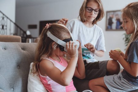 Téléchargez les photos : Trois beaux enfants appréciant les jeux de réalité virtuelle. Heureux amis avec plaisir passer le week-end ensemble à la maison. - en image libre de droit
