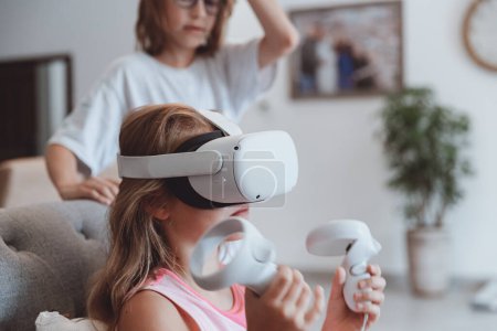 Foto de El hermano mayor le enseña a su hermana pequeña a jugar un videojuego. Adolescentes felices disfrutando de la realidad virtual. Fin de semana divertido en casa. - Imagen libre de derechos