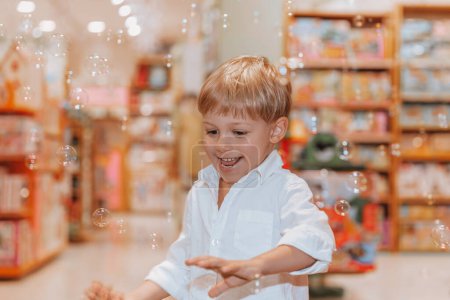 Foto de Un niño lindo está persiguiendo burbujas de jabón. Quiere atraparlos y reventarlos. Diversión infantil. Fiesta de niños en la sala de juegos. - Imagen libre de derechos