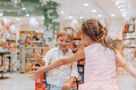 Photo for Cute little brother and sister with pleasure having fun in the toy store with soap bubbles. Playing games with each other. Happy childhood. - Royalty Free Image