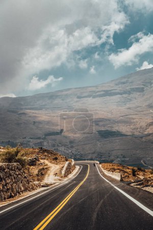 Foto de Conduciendo a lo largo de la carretera entre majestuosas y enormes montañas. La sombra de las nubes deja su huella en las laderas de la montaña. - Imagen libre de derechos