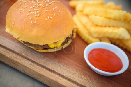 Téléchargez les photos : Hamburger juteux au fromage, frites dorées et sauce rouge. Tous les aliments préférés sont connus dans le monde entier. Aliments riches en calories. - en image libre de droit