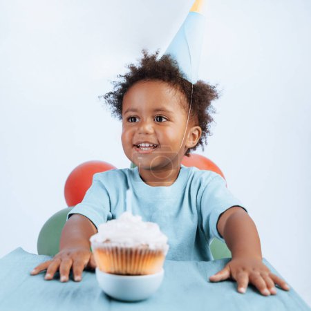 Photo for Portrait of an African-American birthday boy wearing a festive hat with a tasty cake isolated on a white background. Happy celebration concept. - Royalty Free Image