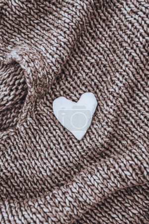 Téléchargez les photos : Un beau fond d'un joli pull en maille marron avec un petit cœur blanc décoratif dessus. Photo conceptuelle de l'amour et de la chaleur. - en image libre de droit