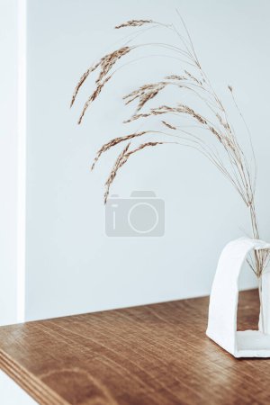 Foto de Un movimiento de diseño muy original, un ramo de trigo maduro en un jarrón blanco sobre la mesa como nota de algo vivo y natural en el interior de la habitación - Imagen libre de derechos
