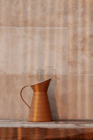 Téléchargez les photos : Pot en bronze de style vintage sur la table en bois sur fond de tuiles beige. Décor de maison à l'ancienne. Solution concepteur. - en image libre de droit