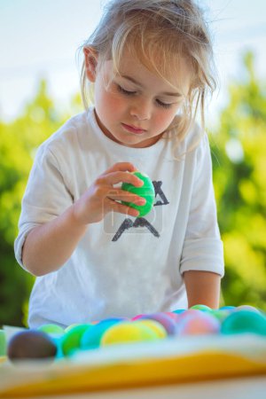 Retrato de un niño serio con un interés considerando hermosos huevos pintados de colores. Disfrutando de la tradición familiar en las felices vacaciones de Pascua.
