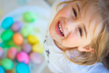 Téléchargez les photos : Portrait d'un mignon petit garçon levant les yeux avec bonheur et espoir. Jouer avec des œufs colorés. Chasse aux œufs. Joyeuses fêtes. - en image libre de droit
