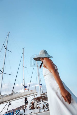 Téléchargez les photos : Une jeune fille en robe blanche douce sur le port près des beaux yachts. Temps ensoleillé vous encourage à sortir à la mer et passer un bon moment. - en image libre de droit