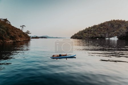 Photo for Peaceful man spending summer vacation in the sea near the mountains. Meditating or sleeping on the sup. Resting among calm water. - Royalty Free Image