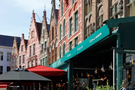 Foto de Bruges, Belgium - September 12, 2022: Colorful brick houses form the frontage of Market Square. There are also enchanting street cafes over which large green, red and black umbrellas are spread out - Imagen libre de derechos