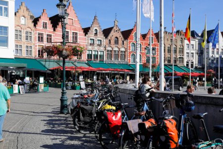 Foto de Bruges, Belgium - September 12, 2022: Colorful brick houses form the frontage of Market Square. There are also enchanting street cafes. Bicycle parking is visible in the square. - Imagen libre de derechos