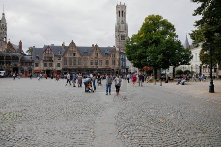 Photo for Bruges, Belgium - September 13, 2022: Outdoor restaurant next to a historic brick building on Burg Square as seen during a cloudy day. A tall, medieval Belfort van Brugge is in the distance - Royalty Free Image