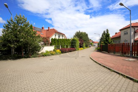 Téléchargez les photos : Jozefoslaw, Poland - June 3, 2020: A narrow, paved street in a housing estate of family houses surrounded by lush vegetation, many plants can also be seen from the street itsel - en image libre de droit