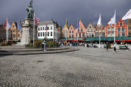 Foto de Bruges, Belgium - September 9, 2022: Colorful brick houses form the frontage of Market Square. There are also enchanting street cafes over which large green, red and black umbrellas are spread ou - Imagen libre de derechos