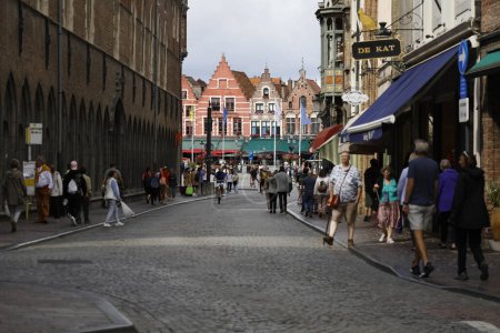 Foto de Brujas, Bélgica - 8 de septiembre de 2022: Una calle empedrada conduce a la Plaza del Mercado, donde en la distancia se pueden ver las fachadas coloridas de las casas y sus caballerizas escalonadas. - Imagen libre de derechos