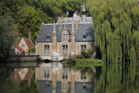 Foto de Brujas, Bélgica - 11 de septiembre de 2022: Una vista en un hermoso parque con el famoso lago Minnewater en el sur de la ciudad. Un edificio de ladrillo con árboles verdes se refleja en el agua del lak - Imagen libre de derechos