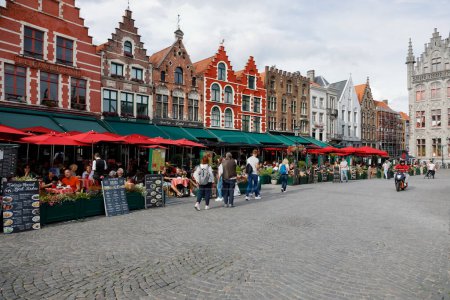 Foto de Brujas, Bélgica - 7 de septiembre de 2022: Coloridas casas de ladrillo con restaurantes al aire libre. Es la plaza más grande de la ciudad, destinada a pasear libremente peatonal - Imagen libre de derechos