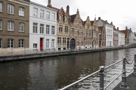 Foto de Brujas, Bélgica - 13 de septiembre de 2022: Casas de ladrillo junto al canal donde el agua en el canal en un día nublado parece estar muy oscura. Hay personas solteras en la distancia - Imagen libre de derechos