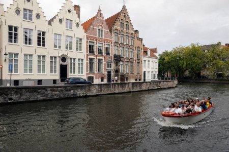 Foto de Brujas, Bélgica - 13 de septiembre de 2022: Casas de ladrillo a lo largo del canal han escalado las caballerizas. Un barco con turistas está navegando a lo largo de la cana - Imagen libre de derechos
