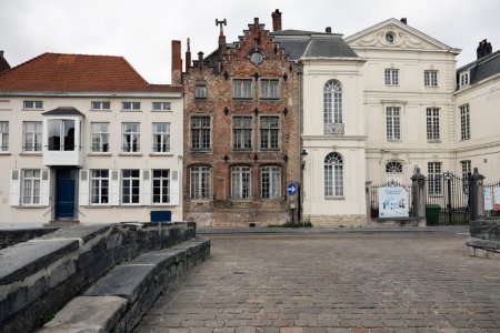 Foto de Brujas, Bélgica - 13 de septiembre de 2022: En una estrecha calle adoquinada, hay una casa histórica con una fachada de ladrillo entre otras casas cuyas fachadas han sido enlucidas. - Imagen libre de derechos