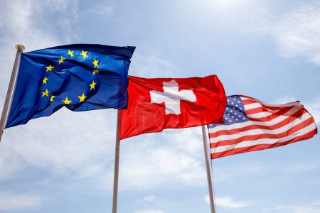 Foto de Tres banderas, la Bandera de Europa, la Bandera de Suiza y la Bandera Nacional de los Estados Unidos, ondean en el viento en Niza, Franco - Imagen libre de derechos