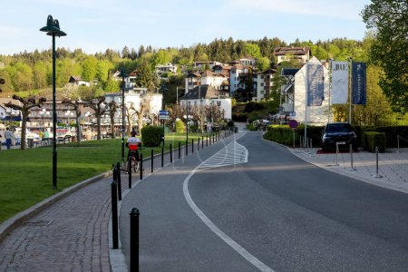 Téléchargez les photos : Velden Am Worthersee, Autriche - 4 mai 2023 : Une route menant aux bâtiments de cette ville, que l'on peut voir un peu plus loin - en image libre de droit