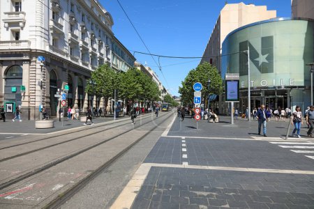 Téléchargez les photos : Nice, France - 3 mai 2023 : Une longue route droite à travers la ville, avec une ligne de tramway qui la longe. Vous pouvez également voir des bâtiments, la nature et beaucoup de gens - en image libre de droit