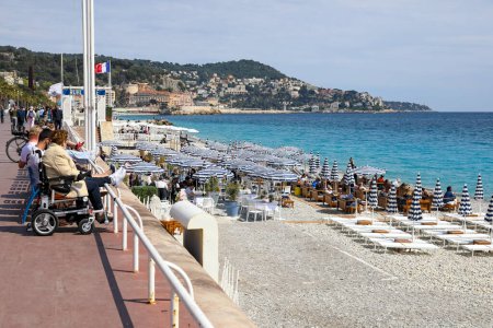 Téléchargez les photos : Nice, France - 21 avril 2023 : Une plage avec des parasols bleu-blanc sur une plage de galets où les baigneurs peuvent se détendre à l'ombre ou au soleil sur la plage de la Promenade des Anglais. - en image libre de droit