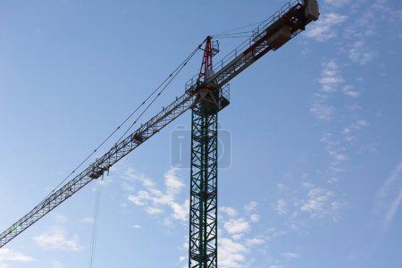 High above the construction site, against the blue sky, you can see the upper part of an industrial machine, a tall tower crane. Construction is taking place in the Goclaw housing estate in Warsaw