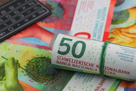 Photo for A roll of Swiss franc banknotes, other Swiss paper money and a calculator. CHF paper money. This theme can be used to illustrate many different financial topics. - Royalty Free Image