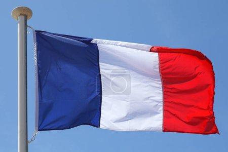 The flag of France waves on a flagpole against a blue sky on a sunny day