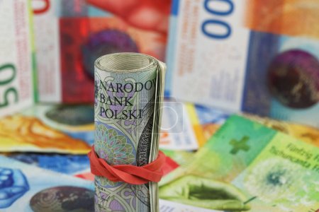 Eine Rolle polnischer Banknoten wird gegen die flachen Schweizer Franken-Banknoten gezeigt. CHF, PLN Papiergeld. Dieses Thema kann verwendet werden, um viele verschiedene Finanzthemen zu illustrieren.