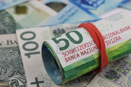 Eine Rolle Schweizer Franken-Banknoten wird gegen die flachen polnischen Zloty-Banknoten gezeigt. CHF, PLN Papiergeld. Dieses Thema kann verwendet werden, um viele verschiedene Finanzthemen zu illustrieren