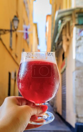 Photo for Glass of a raspberry Lambic ale at an outdoor restaurant with a background of blurred buildings in old town or Vieille Ville in Nice, South of France - Royalty Free Image