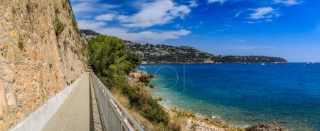 Panorama with a path along Mediterranean Sea, view of Roquebrune Cap Martin peninsula and turquoise water at a beach near Monaco, South of France