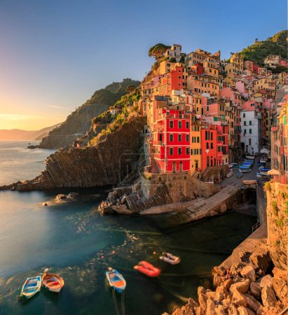 Sunset view onto the Mediterranean Sea with traditional boats and colorful houses in old town of Riomaggiore in Cinque Terre, Italy