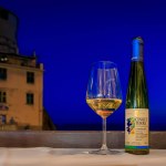 Manarola, Italy - May 31, 2022: Bottle and glass of traditional Cinque Terre Sciacchetra sweet white wine at a restaurant with Mediterranean sea view