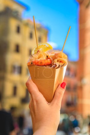 Main tenant un cône de fritto misto, cuisine de rue italienne mélange de calamars frits et crevettes avec des maisons colorées à Riomaggiore, Cinque Terre Italie