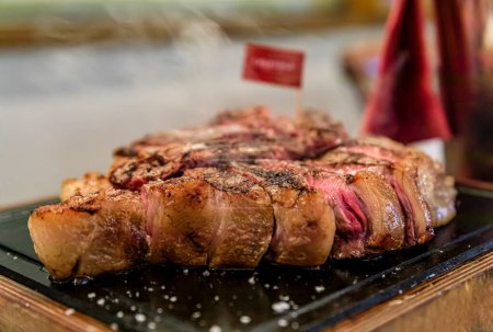 Photo for Classic seared dry aged T-bone Florentine steak from a Chianina cow steaming on a grill serving plate at a restaurant in Florence, Italy - Royalty Free Image