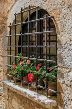 Photo for Metal bars and potted flowers on an arched old stone house window in the medieval town of Saint Paul de Vence, French Riviera, South of France - Royalty Free Image