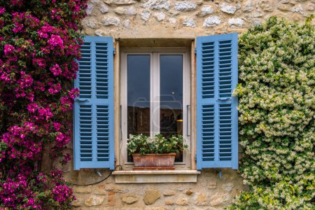 Photo for Bougainvilia and jasmine flower vines framing an old stone house window in the medieval town of Saint Paul de Vence, French Riviera, South of France - Royalty Free Image