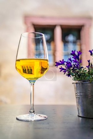Foto de Una copa de vino blanco local en un restaurante al aire libre con casas borrosas de entramado de madera en Riquewihr, Francia, un pueblo en la Ruta del Vino de Alsacia - Imagen libre de derechos