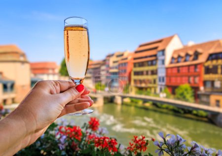 Photo for Woman s hand with a glass of Cremant sparkling wine at a winstub restaurant with flowers in the background, Petite France district, Strasbourg, France - Royalty Free Image