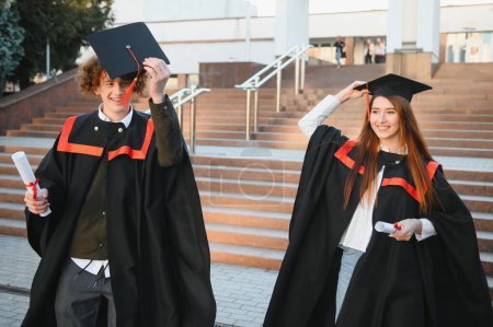Foto de Graduados en mantillas con diplomas en las manos están de pie cerca de la universidad - Imagen libre de derechos