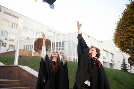 Foto de Graduados en mantillas con diplomas en las manos están de pie cerca de la universidad - Imagen libre de derechos