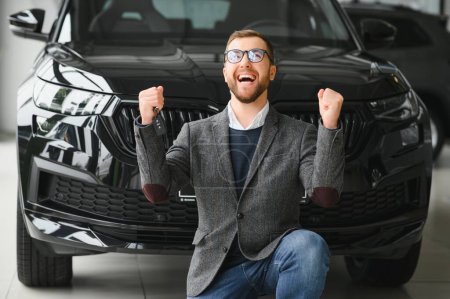 Happy owner of a new car. Emotional handsome man in casual clothes is happy, buying a car in the dealership