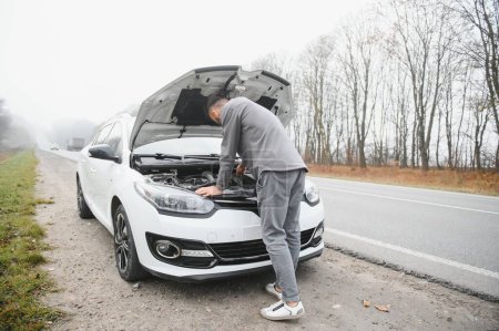 young stressed man having trouble with his broken car looking in frustration at failed engine.